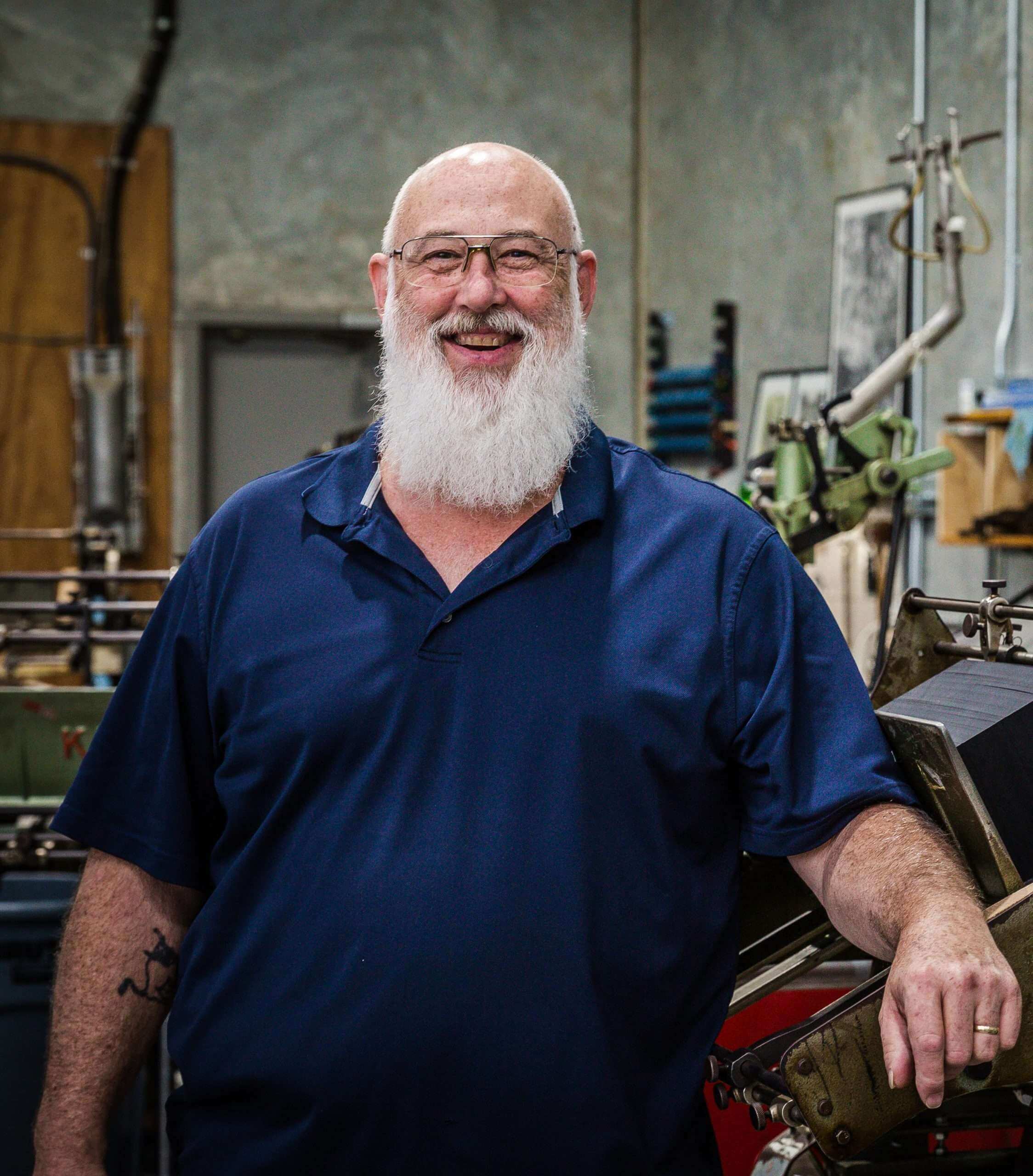 Letterpress printer with white beard standing in front of a machine